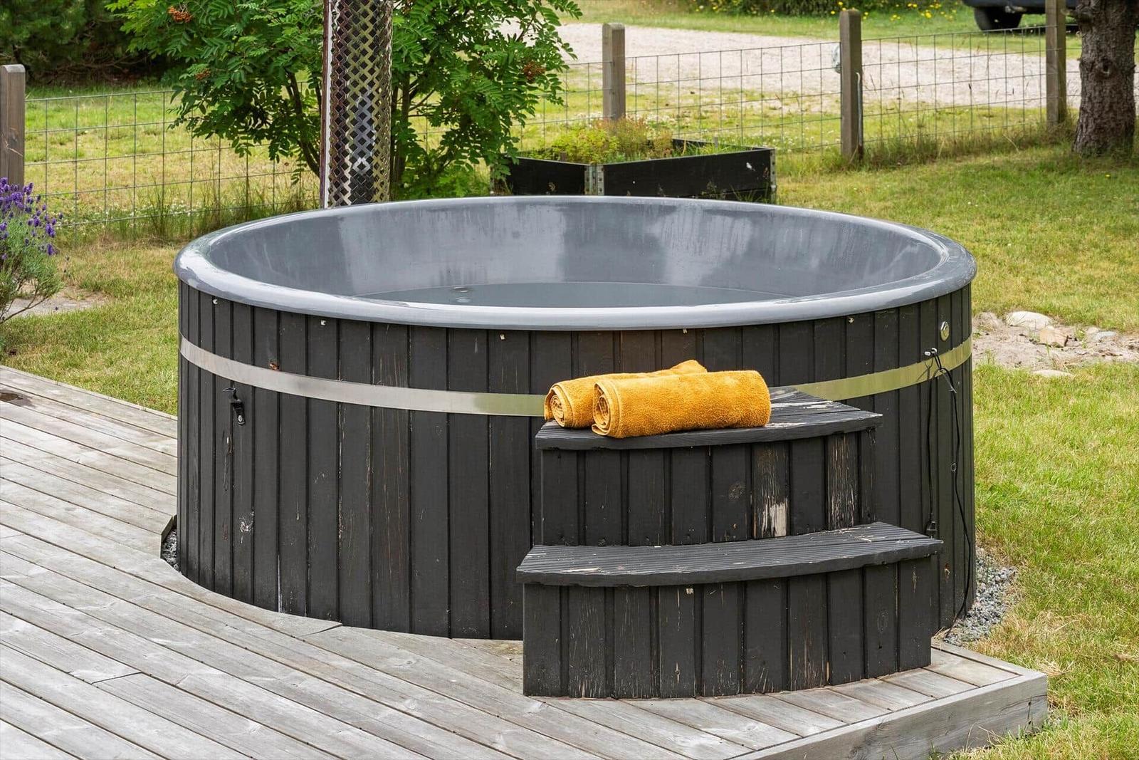 Schwarzer Whirlpool mit Holzstufen und gelben Handtüchern auf Terrasse.
