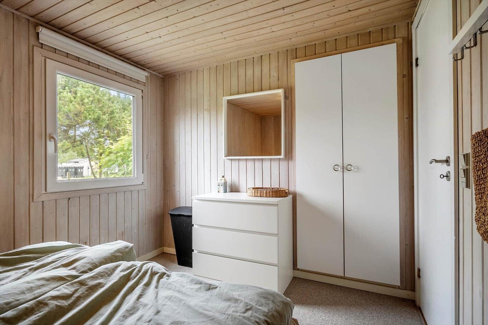 Schlafzimmer mit Holzwand, Fenster, Schrank und Schminktisch.