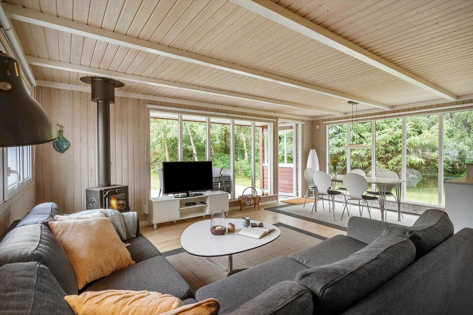 Wohn- und Essbereich mit Holzdecke, Sofa, TV und großflächigen Fenstern zur Aussicht.