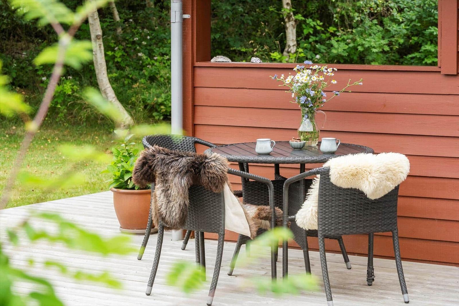 Terrasse mit Tisch, Stühlen und Blumen vor rotem Holzhaus.