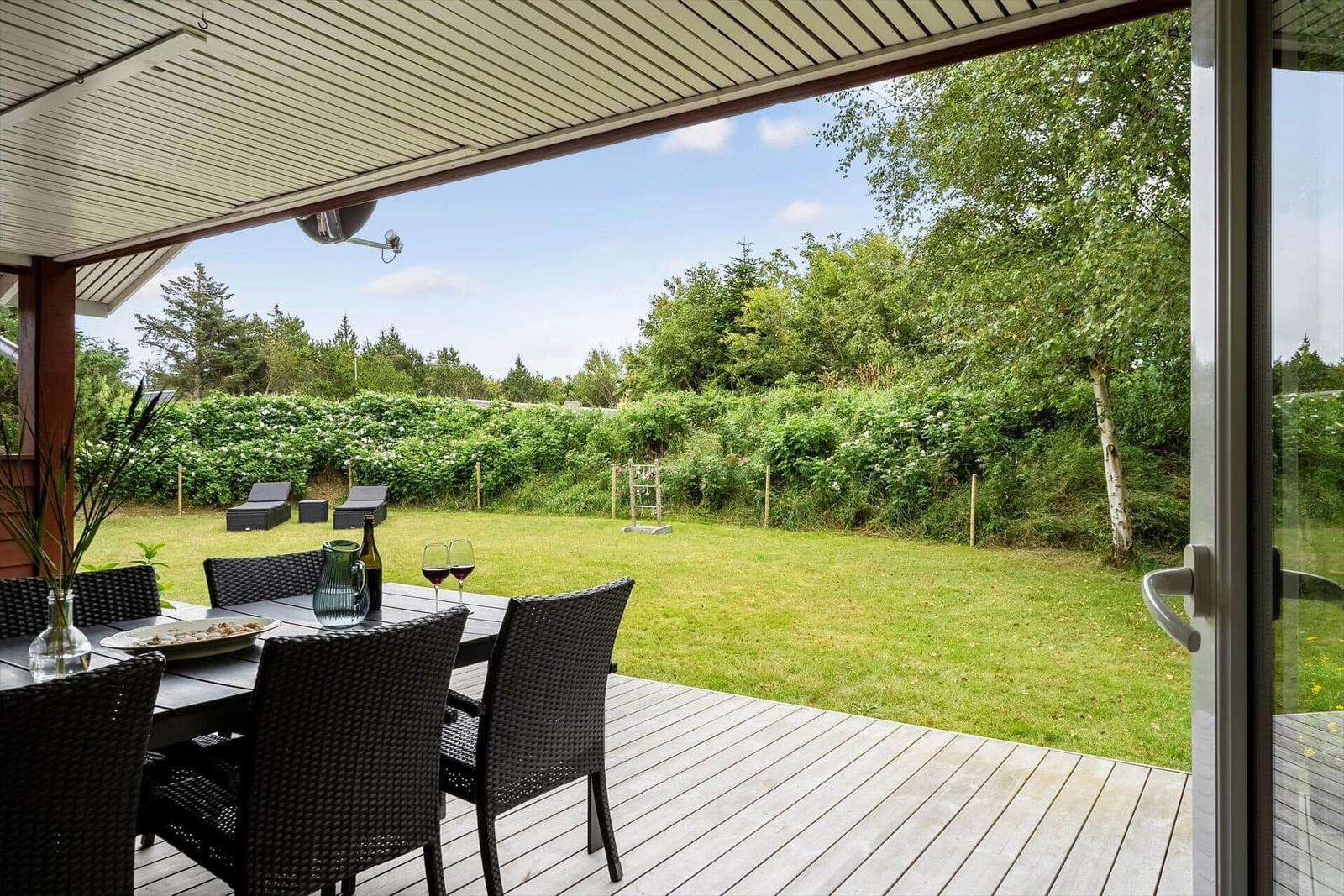 Terrasse mit Tisch und Stühlen, Blick auf grünen Garten und Bäume.