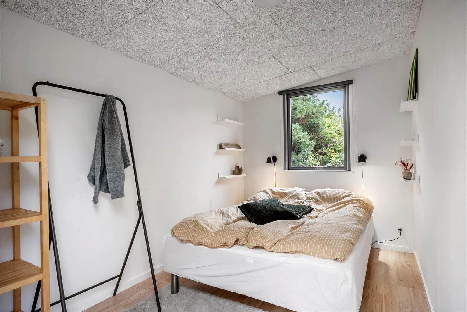 Schlafzimmer mit Bett, Kleiderständer und Fenster zur grünen Außenseite.