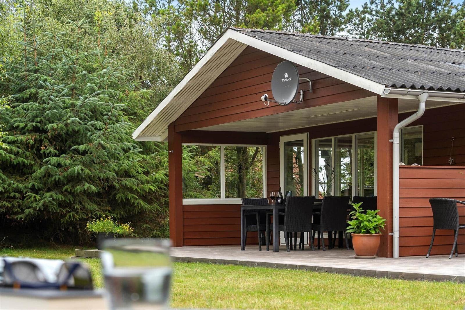Haus mit Terrasse, Sitzgelegenheit und Satellitenantenne. Umgeben von Bäumen und Gras.