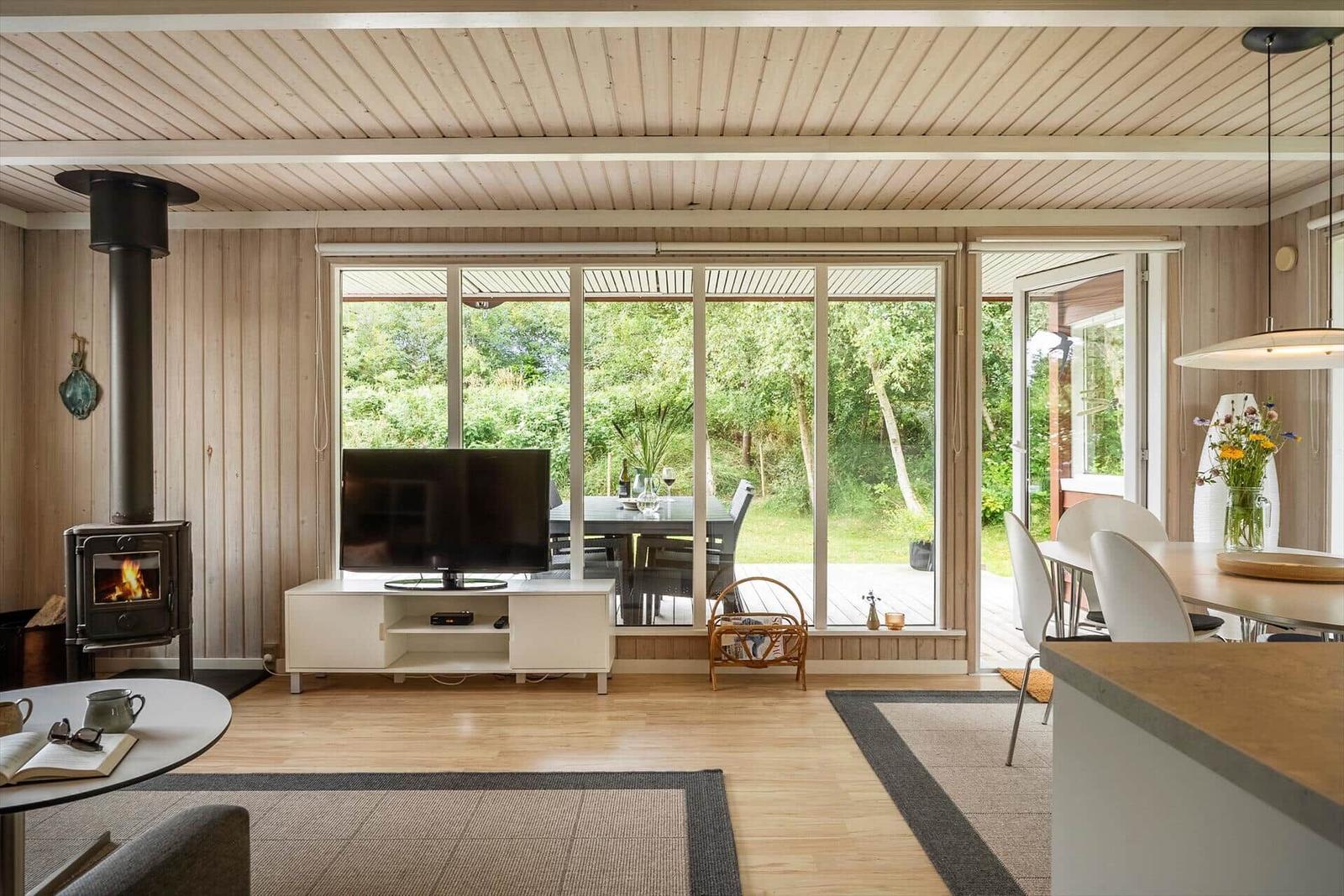 Wohn- und Essbereich mit Holzdecke, Kamin und großem Fenster zum Garten.