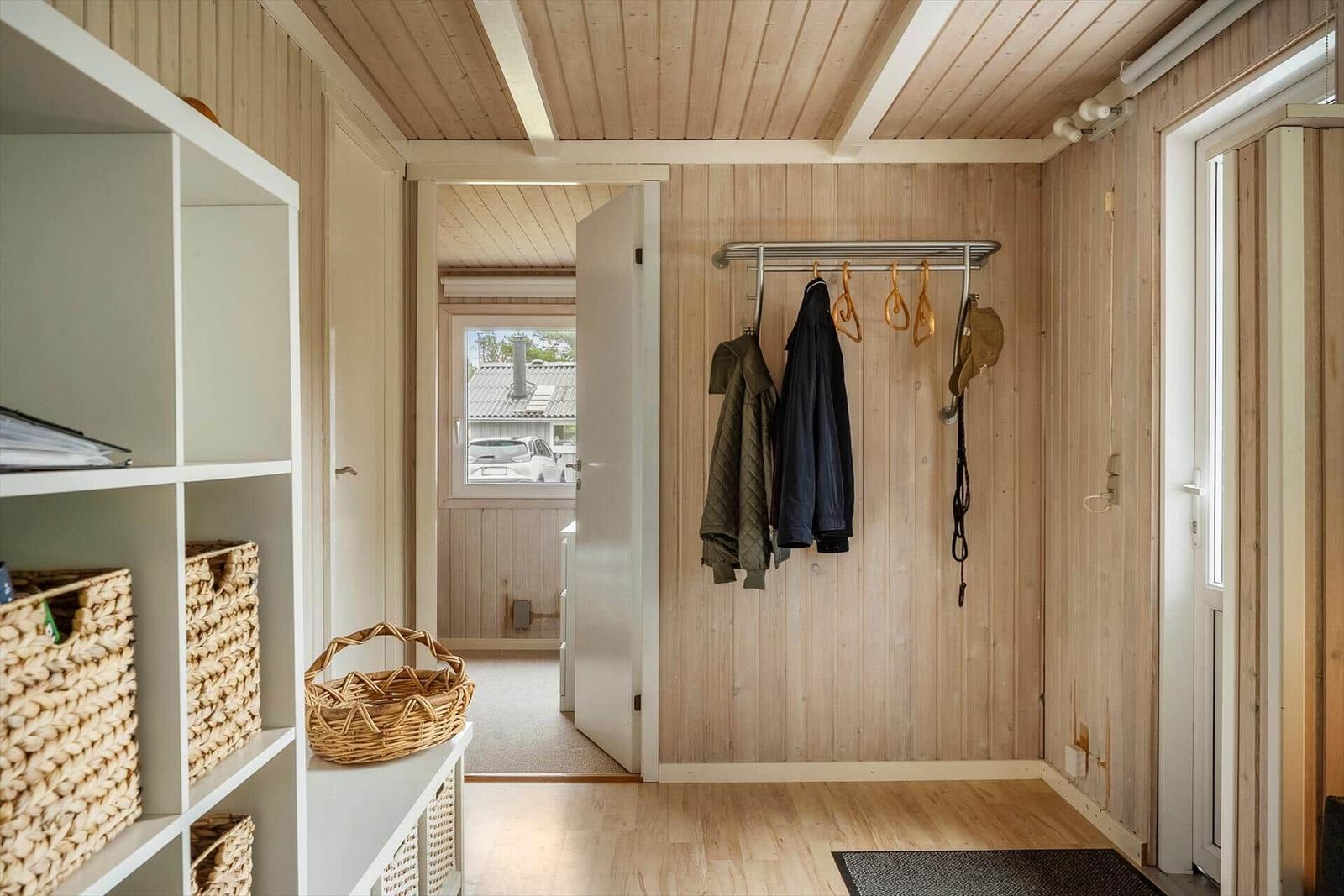 Eingangsbereich mit Kleiderständer, Wickerkörben und Holzwandverkleidung.
