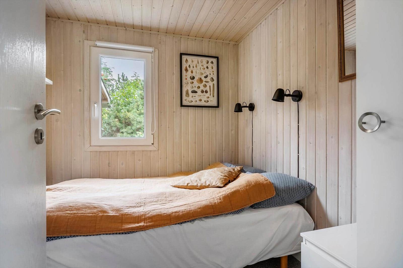 Schlafzimmer mit Holzwand, Bett und Fenster mit Blick auf Grün.