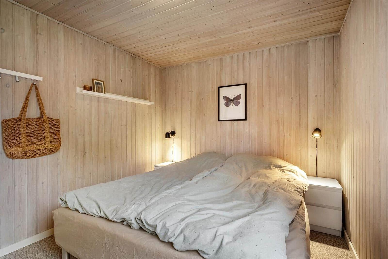 Schlafzimmer mit Holzwand, Bett, Nachttisch und Wandbild.