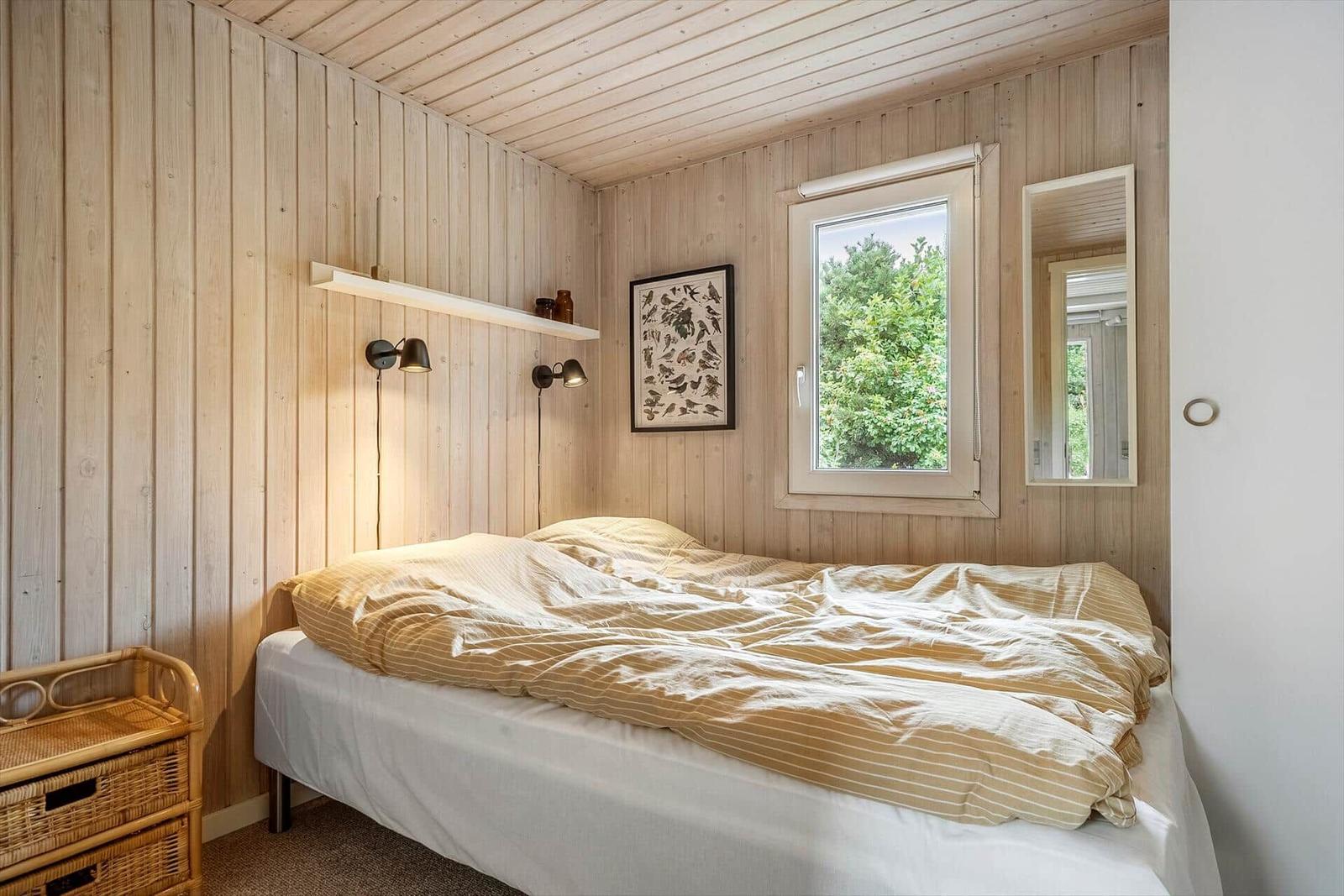 Schlafzimmer mit Holzwand, Bett, Fenster und Spiegel.