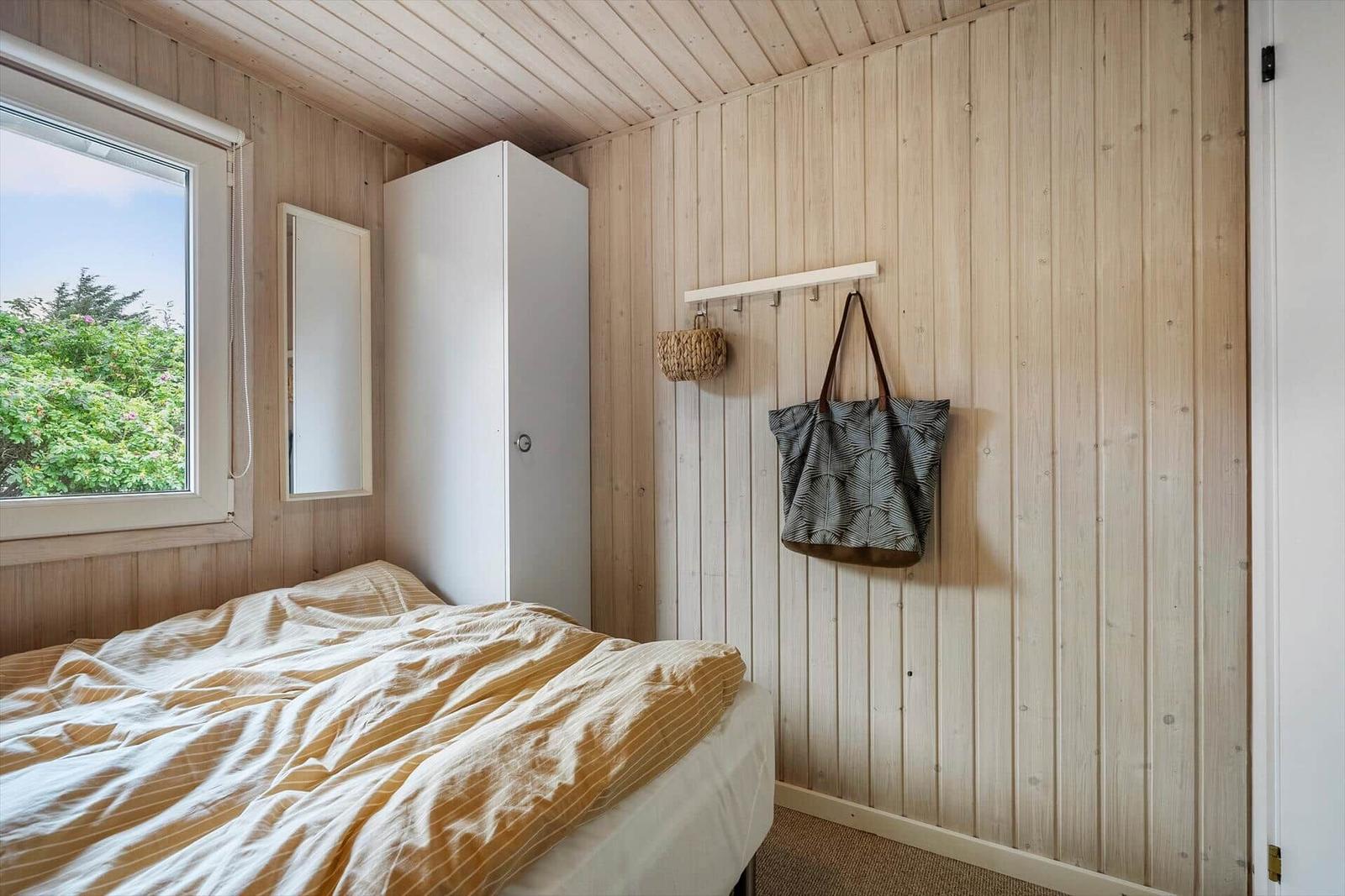 Schlafzimmer mit Holzwand, Bett, Kleiderständer und Fenster.
