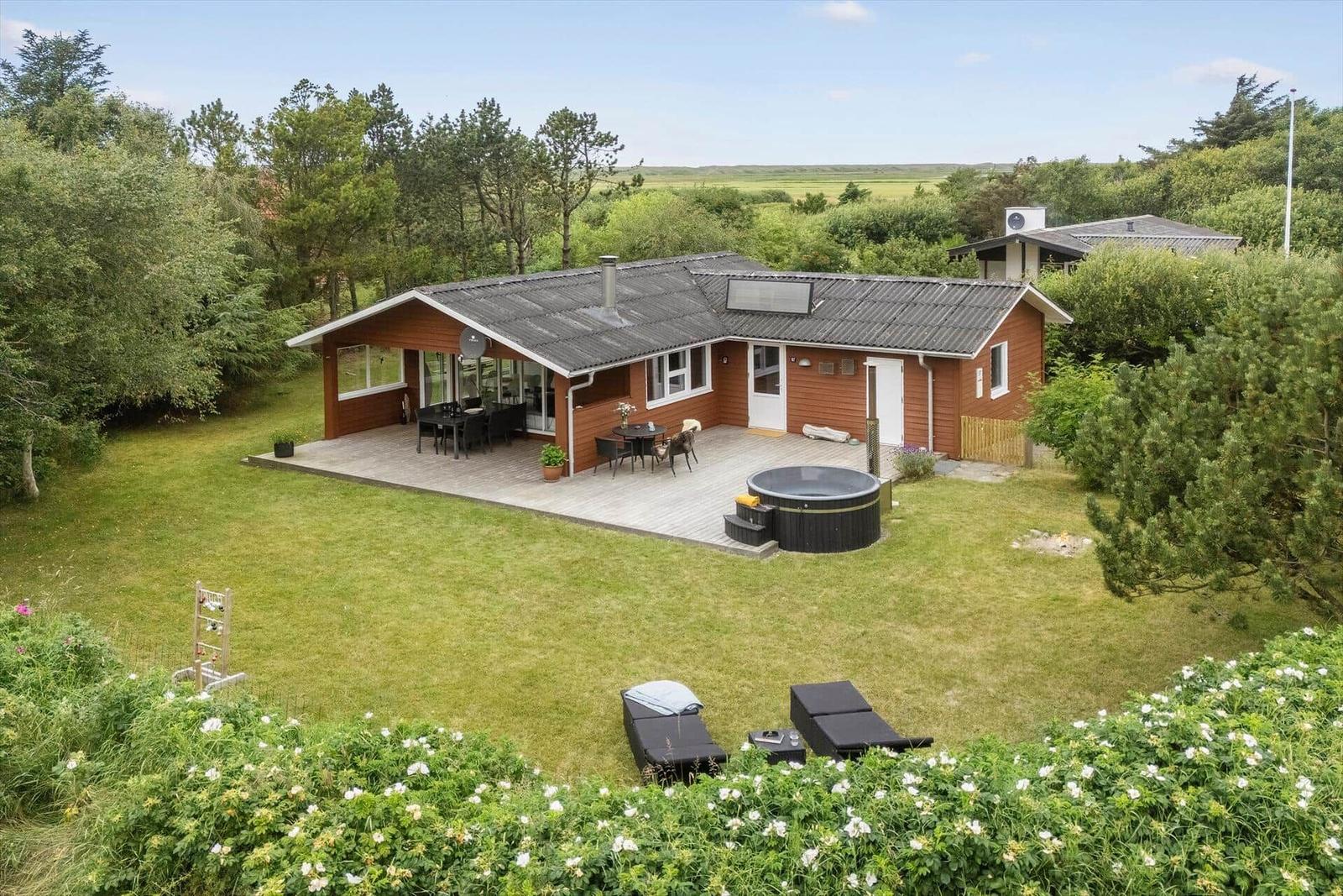 Haus mit Terrasse, Whirlpool und Garten. Umgeben von Bäumen und Gras.