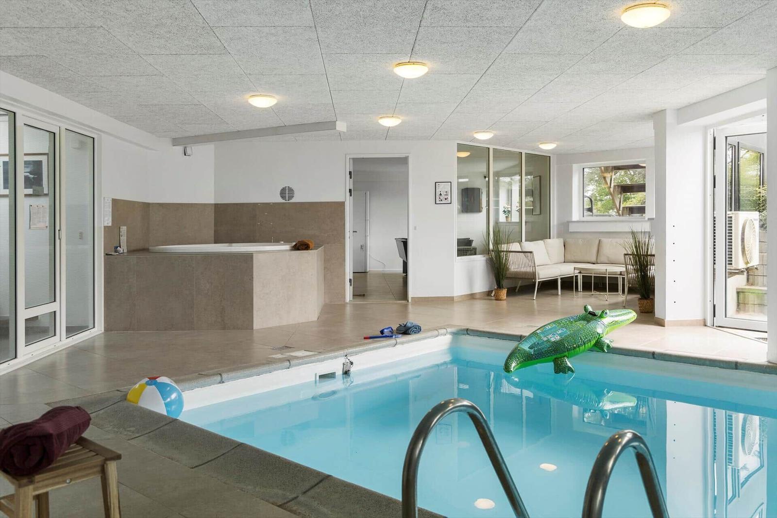 Indoorpool mit Whirlpool und Sitzbereich. Grünliches Krokodil auf dem Wasser.