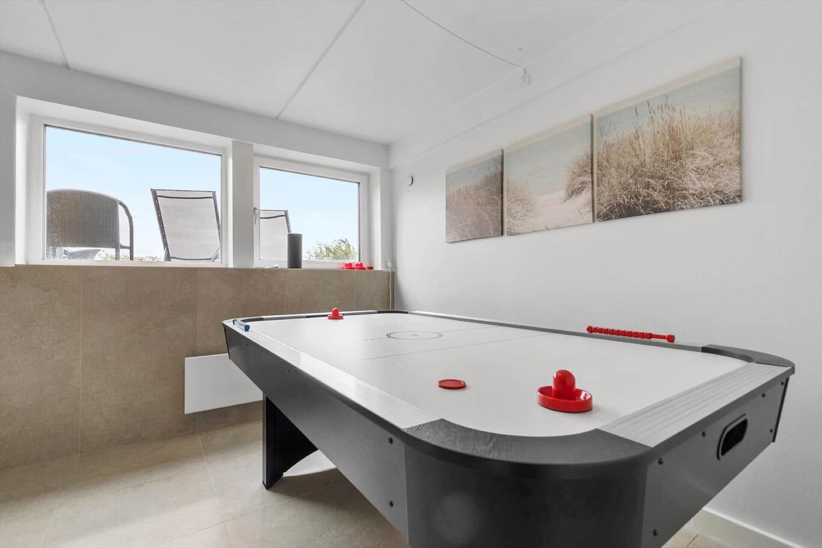 Ein Raum mit Airhockey-Tisch, Fenstern und Strandbildern an der Wand.