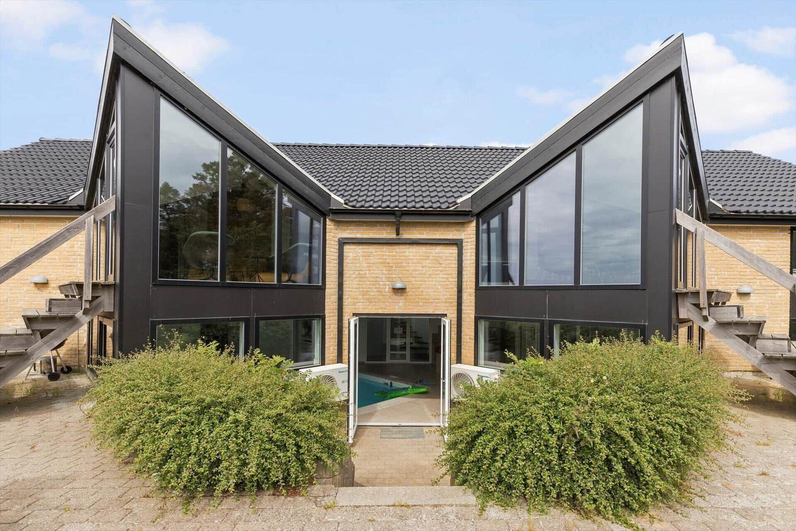 Moderne Villa mit Pool und großzügigen Fenstern. Holzstufen und grüne Hecken.