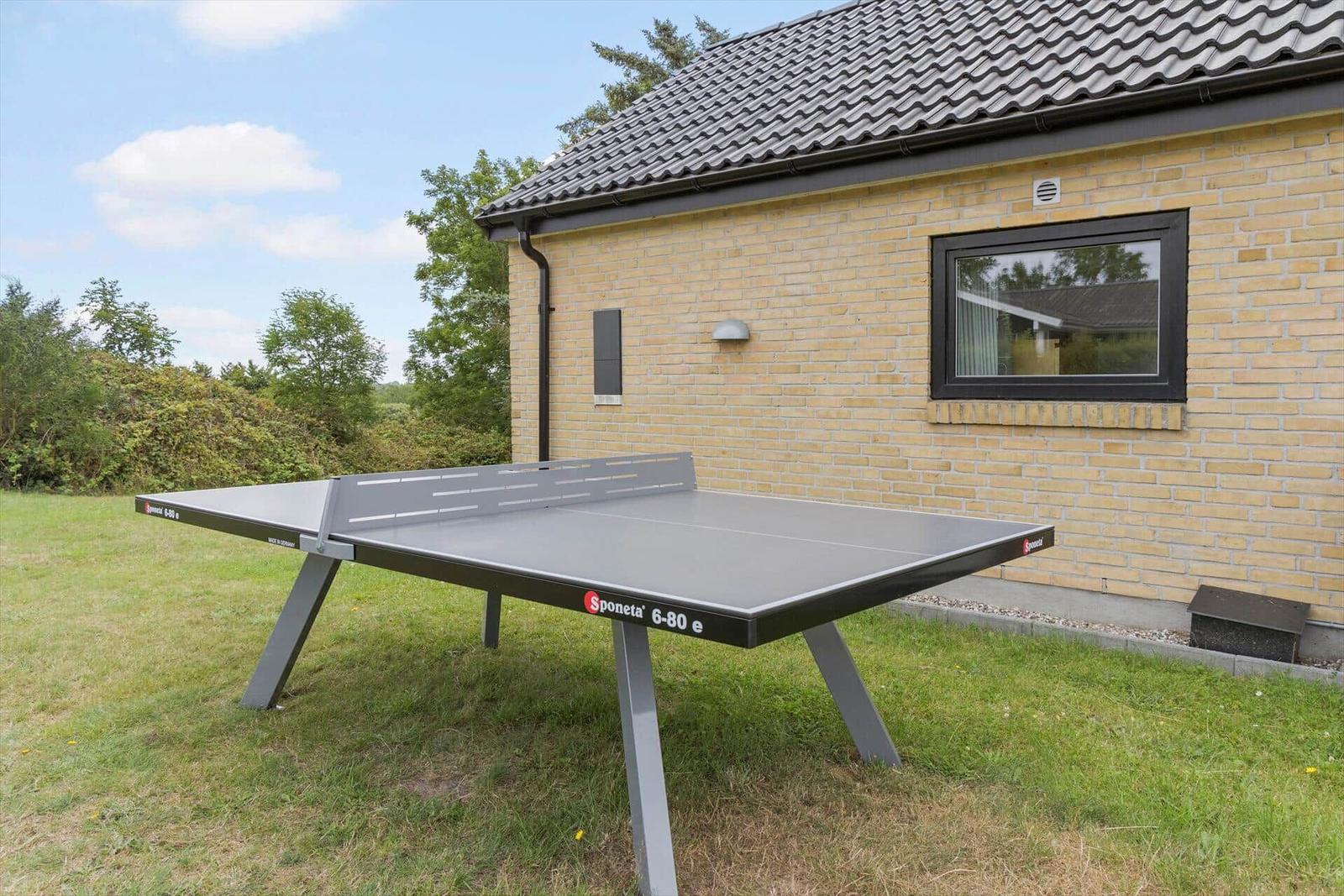 Tischtennisplatte im Garten vor einem Haus mit Backsteinwand und Dach.