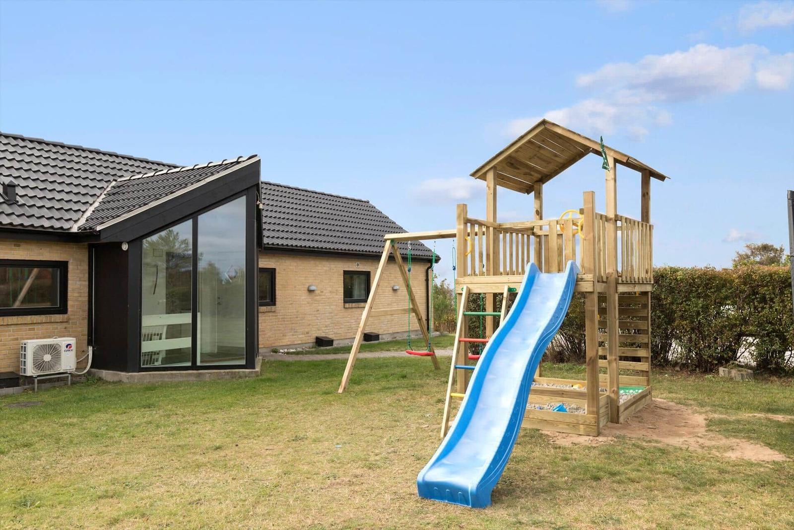 Haus mit Spielplatz, blauer Rutsche und Schaukel im Garten.