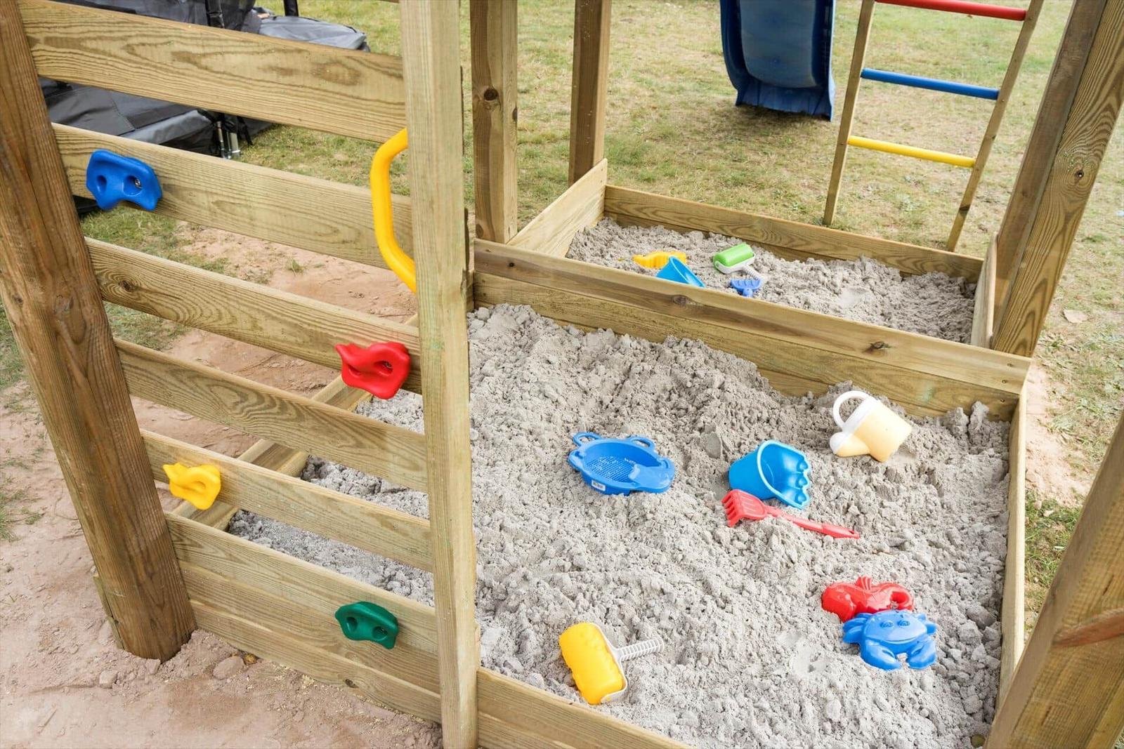 Holzspielplatz mit Sandkasten und bunten Kinderspielzeugen