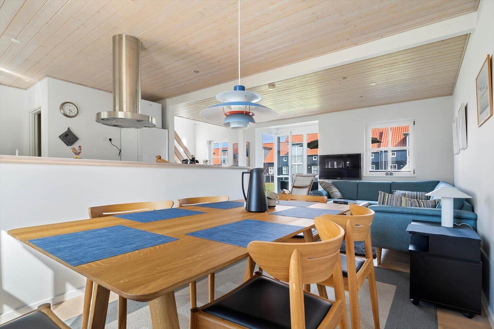 Essbereich mit Holztisch und Stühlen, blauen Tischdecken und Wohnzimmer im Hintergrund.