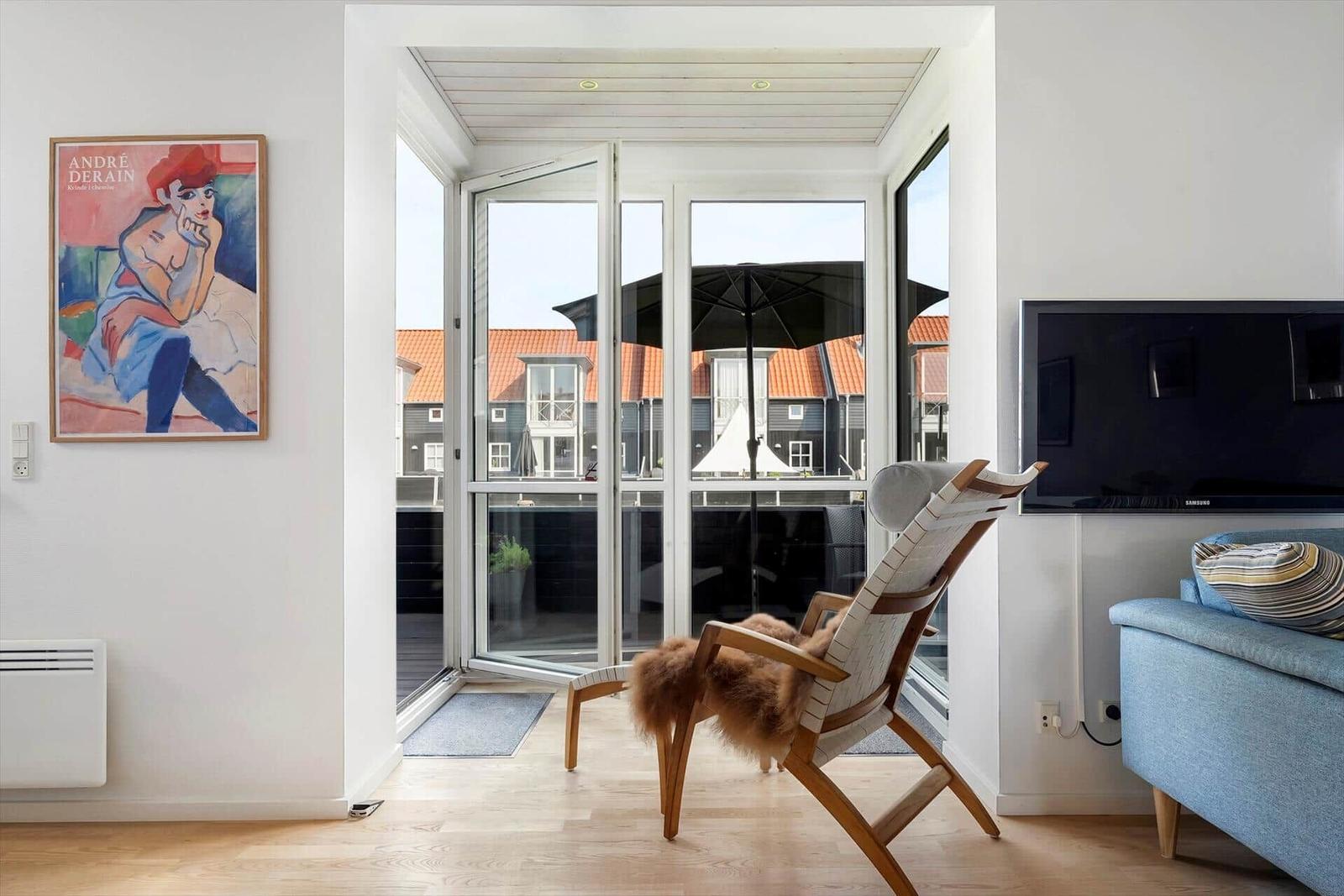 Wohnzimmer mit Sessel, Fernseher und Blick auf Balkon mit Sonnenschirm.