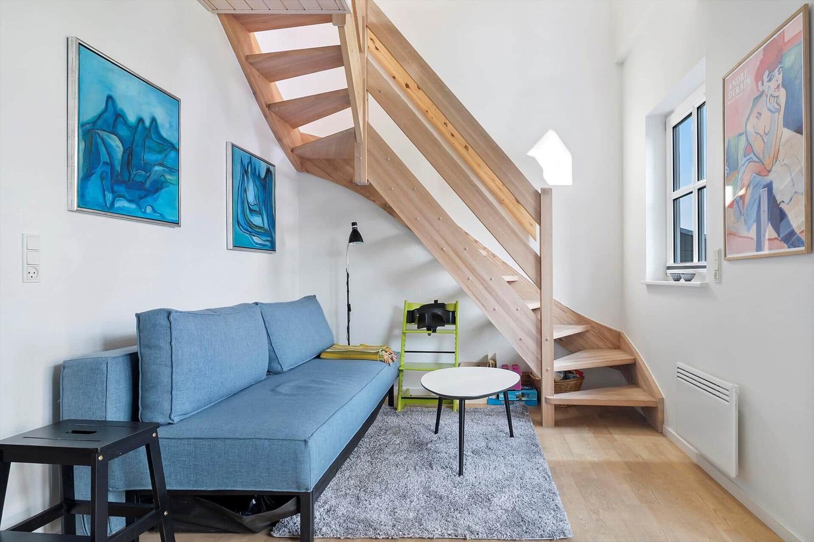 Ein Wohnzimmer mit blauem Sofa, Holztreppe und Wandbildern.