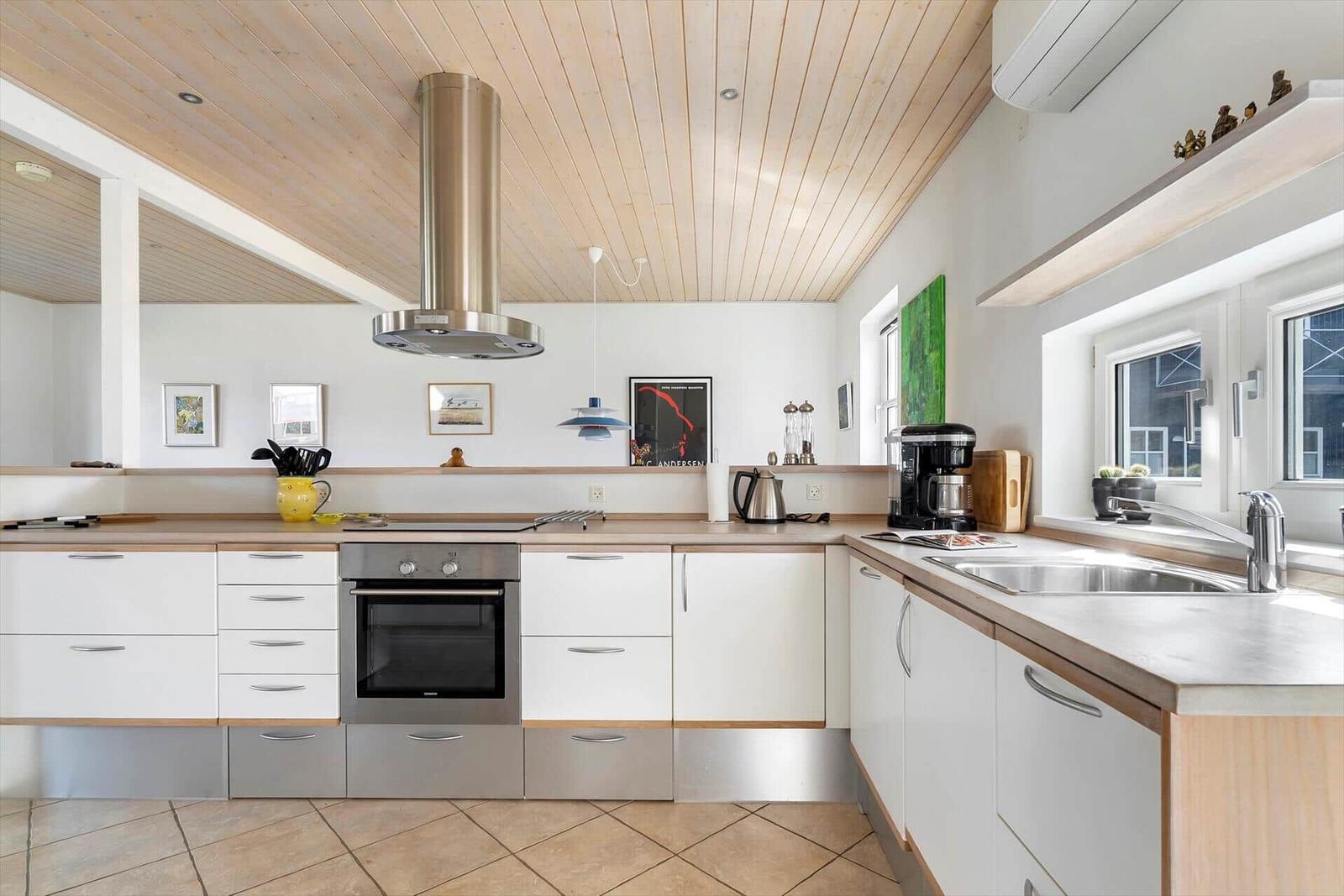 Küche mit weißen Schränken, Holzoberflächen und Edelstahlgeräten unter Holzdecke.