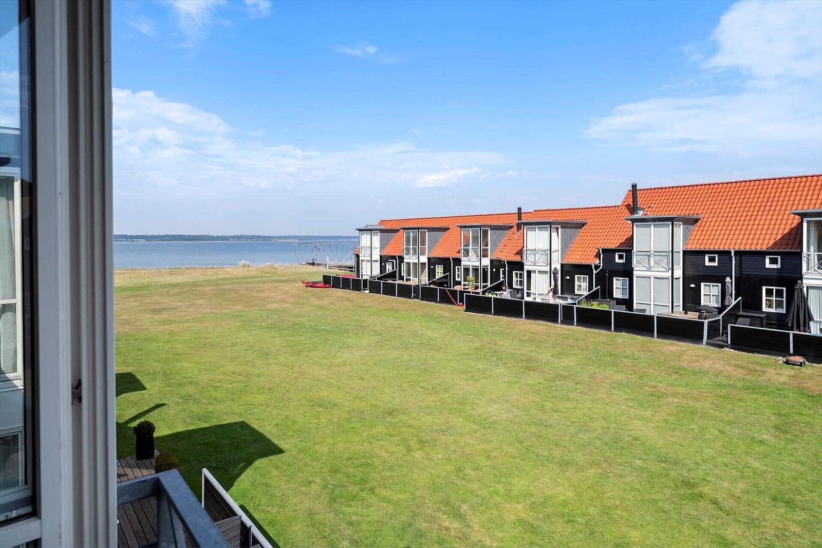 Ausblick auf Grünfläche, Wasser und moderne Häuser mit roten Dächern.