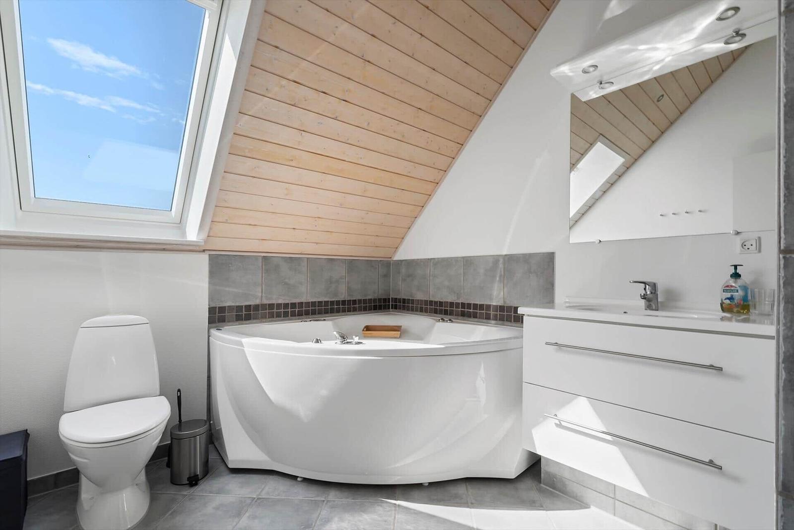 Bad mit Whirlpool, Toilette und Waschbecken unter Holzdecke mit Dachfenster.