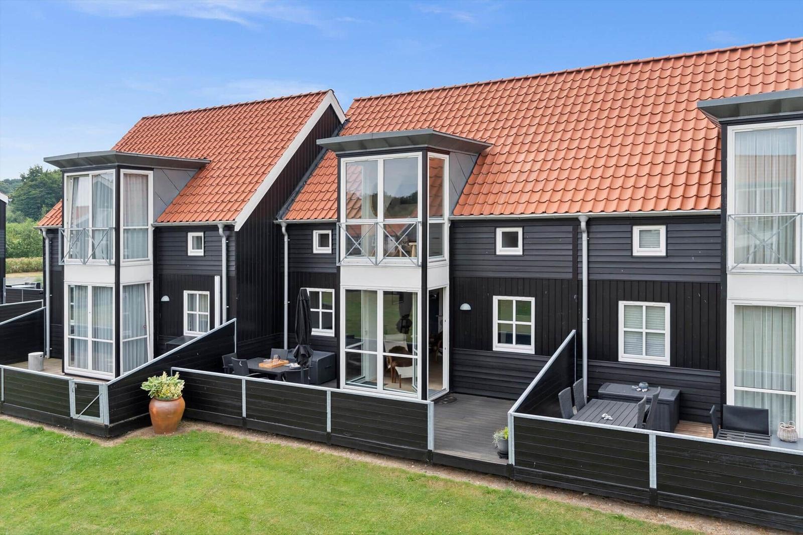 Schwarze Holzhäuser mit roten Dächern und Terrassen mit Gartenmöbeln.