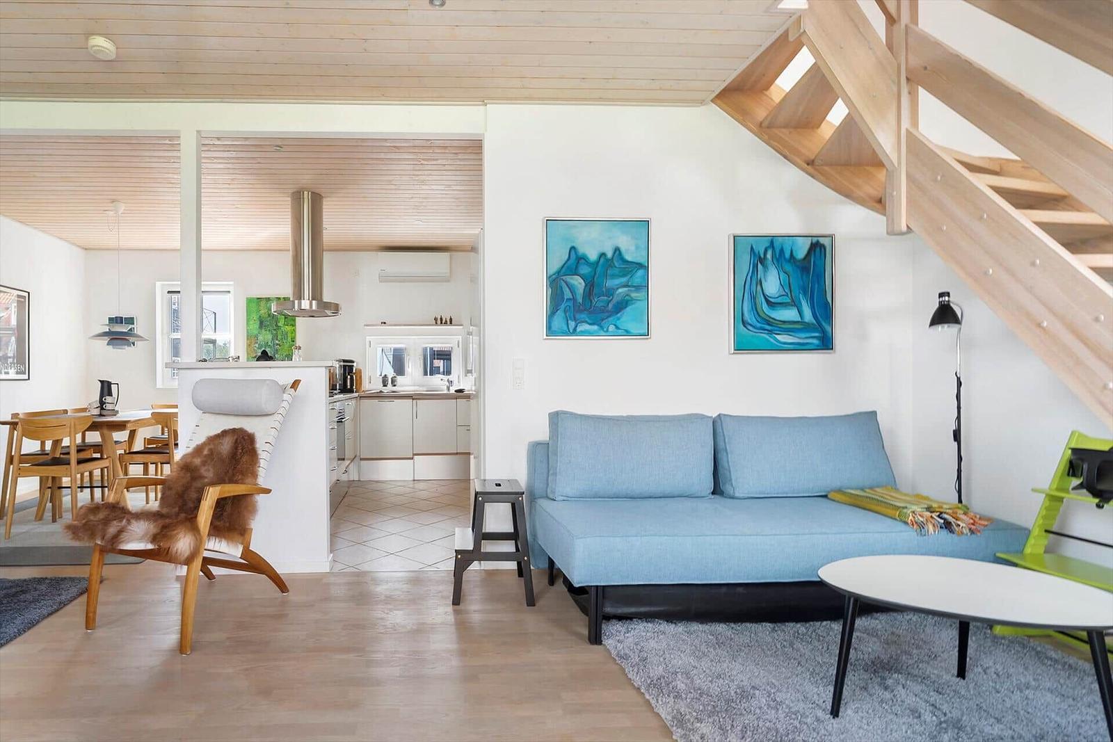 Wohnzimmer mit Sofa, Tisch und Stuhl. Küche und Essbereich sind sichtbar. Holzdecke und Treppenhaus.