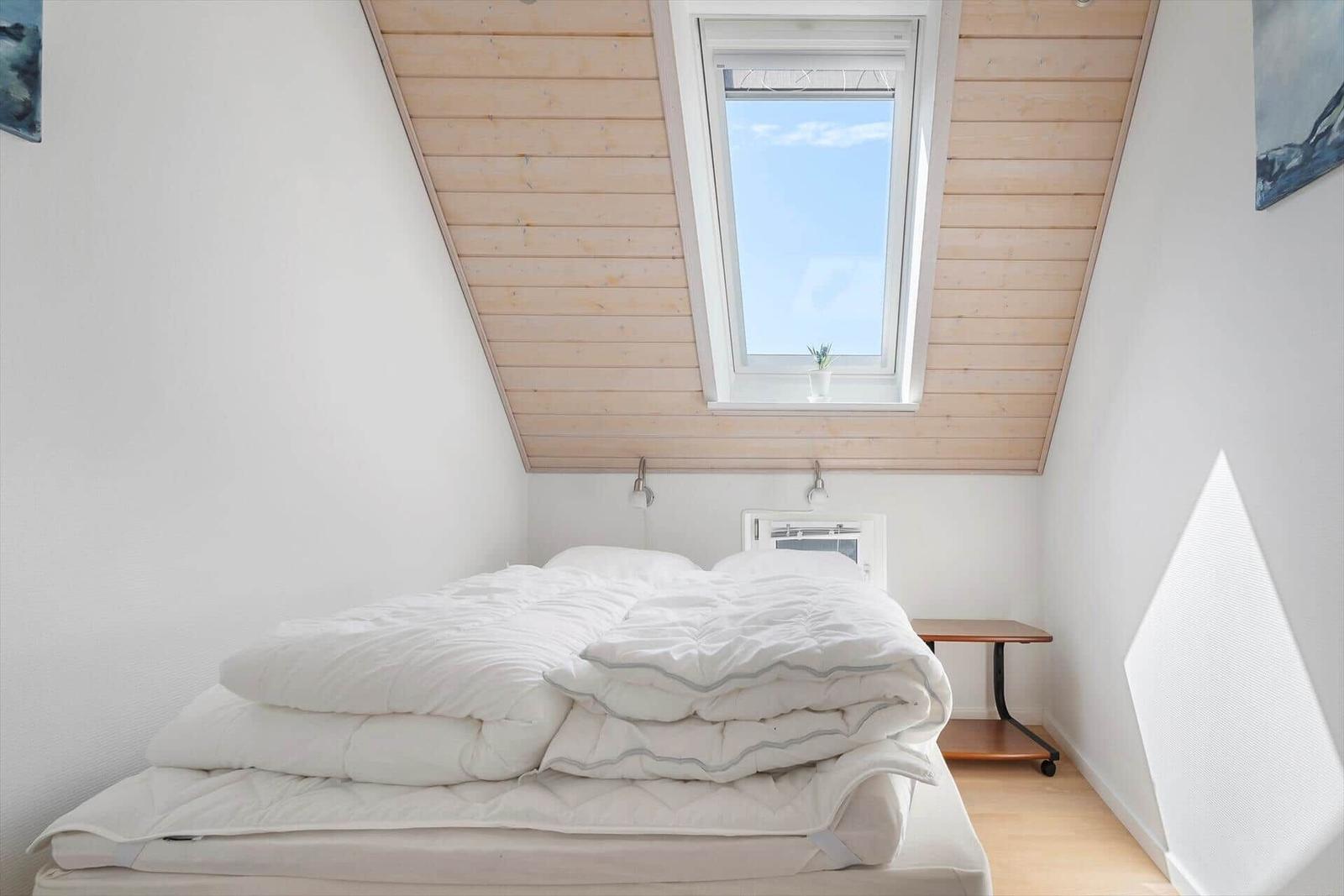 Schlafzimmer mit Dachfenster, Bett und Nachttisch.