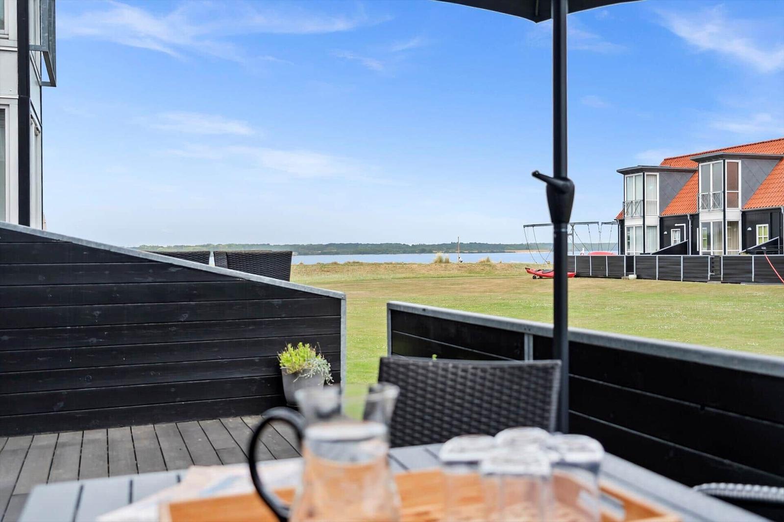 Terrasse mit Tisch und Stühlen, Blick auf Grünfläche und Wasser.