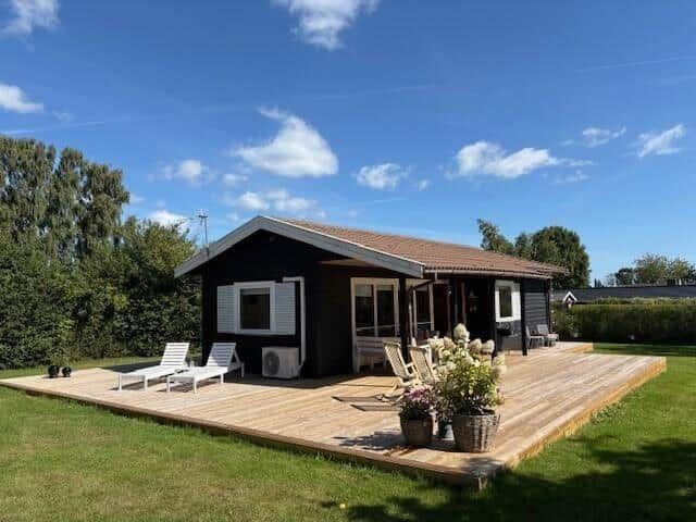 Wooden terrace with loungers and flowers in front of a small house with roof and windows.