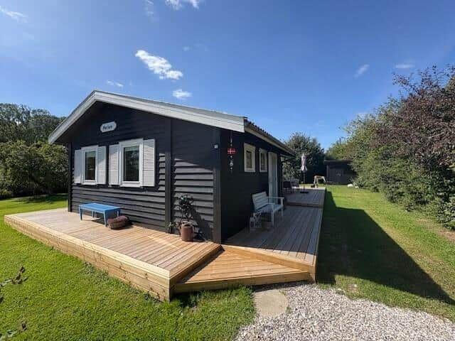 Black wooden house with deck and garden. Single windows and doors.