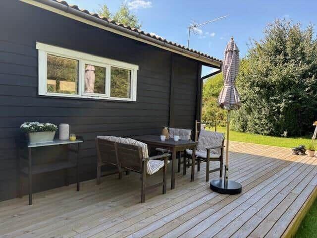 Deck with table, chairs, and umbrella beside dark brown house.