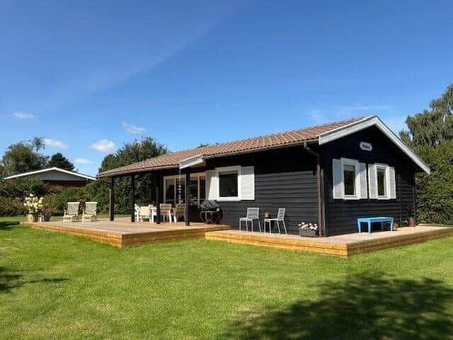 Black cabin with wooden terrace and garden. Outdoor seating and barbecue area.