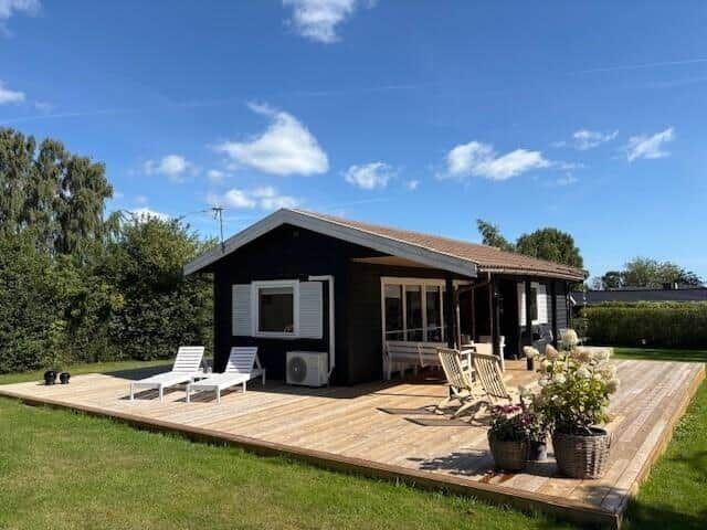 Black cabin with wooden terrace, loungers, and garden.
