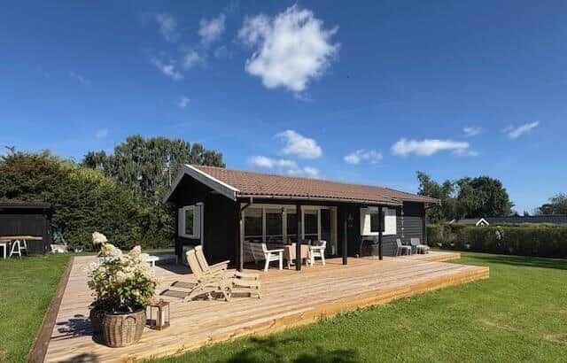 Wooden terrace with seating in front of a modern garden house under blue sky.