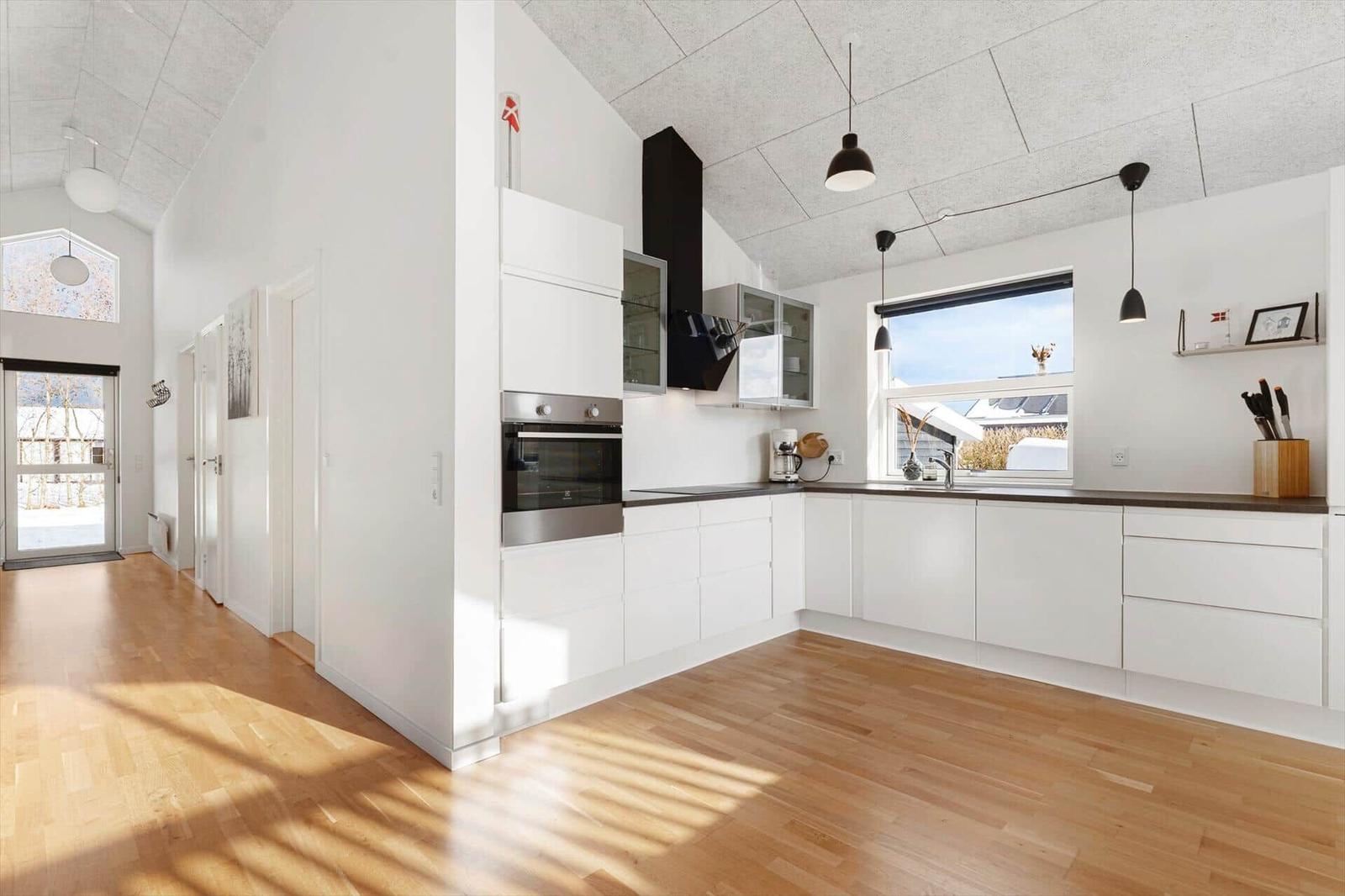 Moderne Küche mit weißen Schränken, Holzboden und Fenster. Küchenzeile mit Spüle und Dunstabzug.