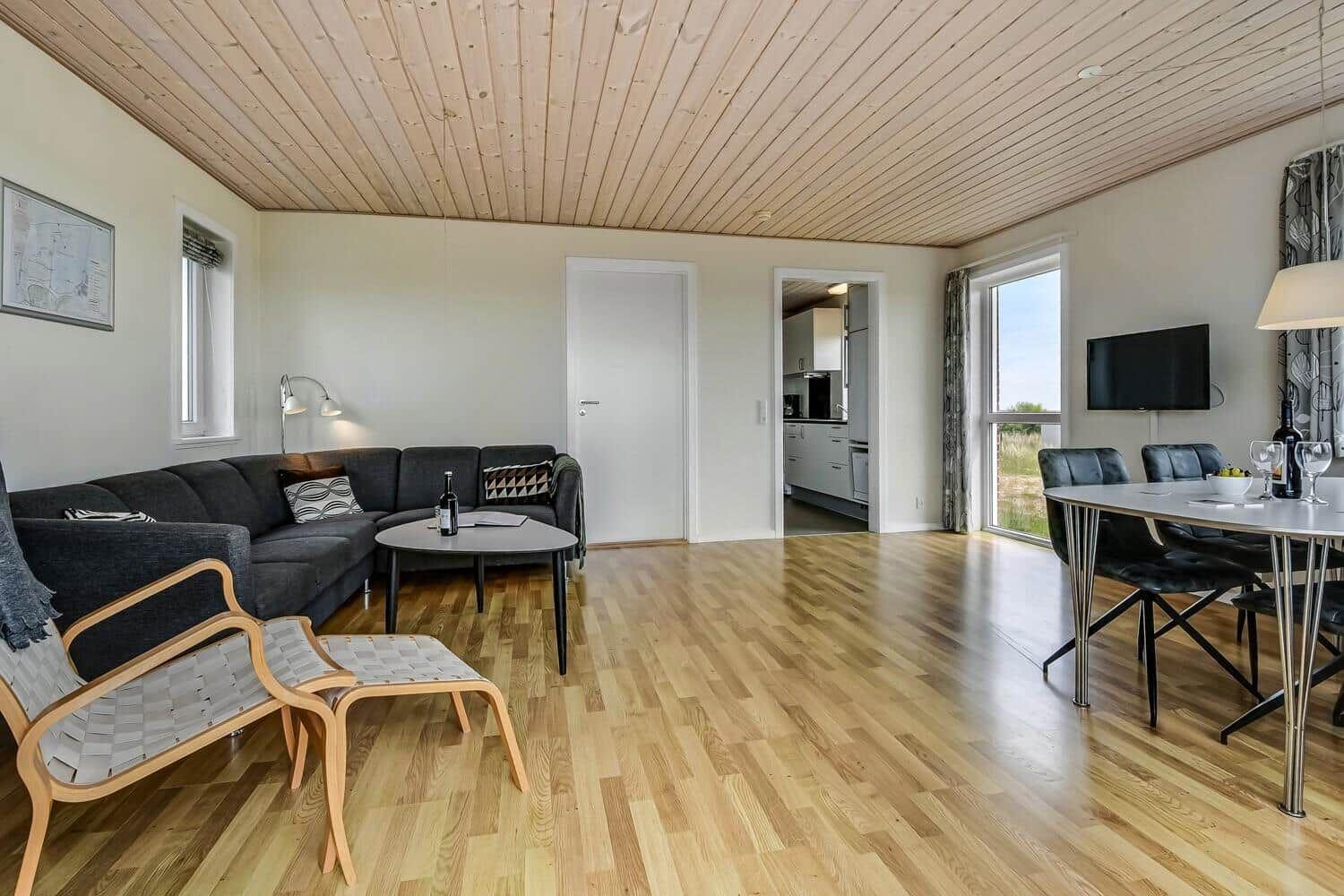 Wohn- und Essbereich mit Holzboden, Sofa, Esstisch und Küche im Hintergrund.