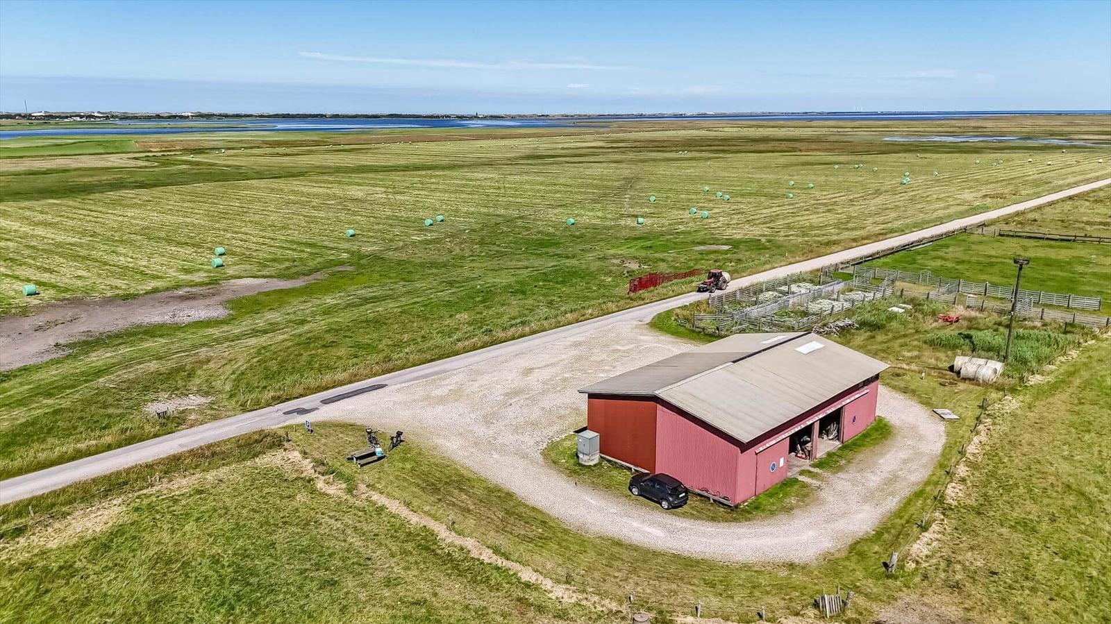 Roter Scheunenbau mit Garage und umliegenden Feldern mit Heuballen.