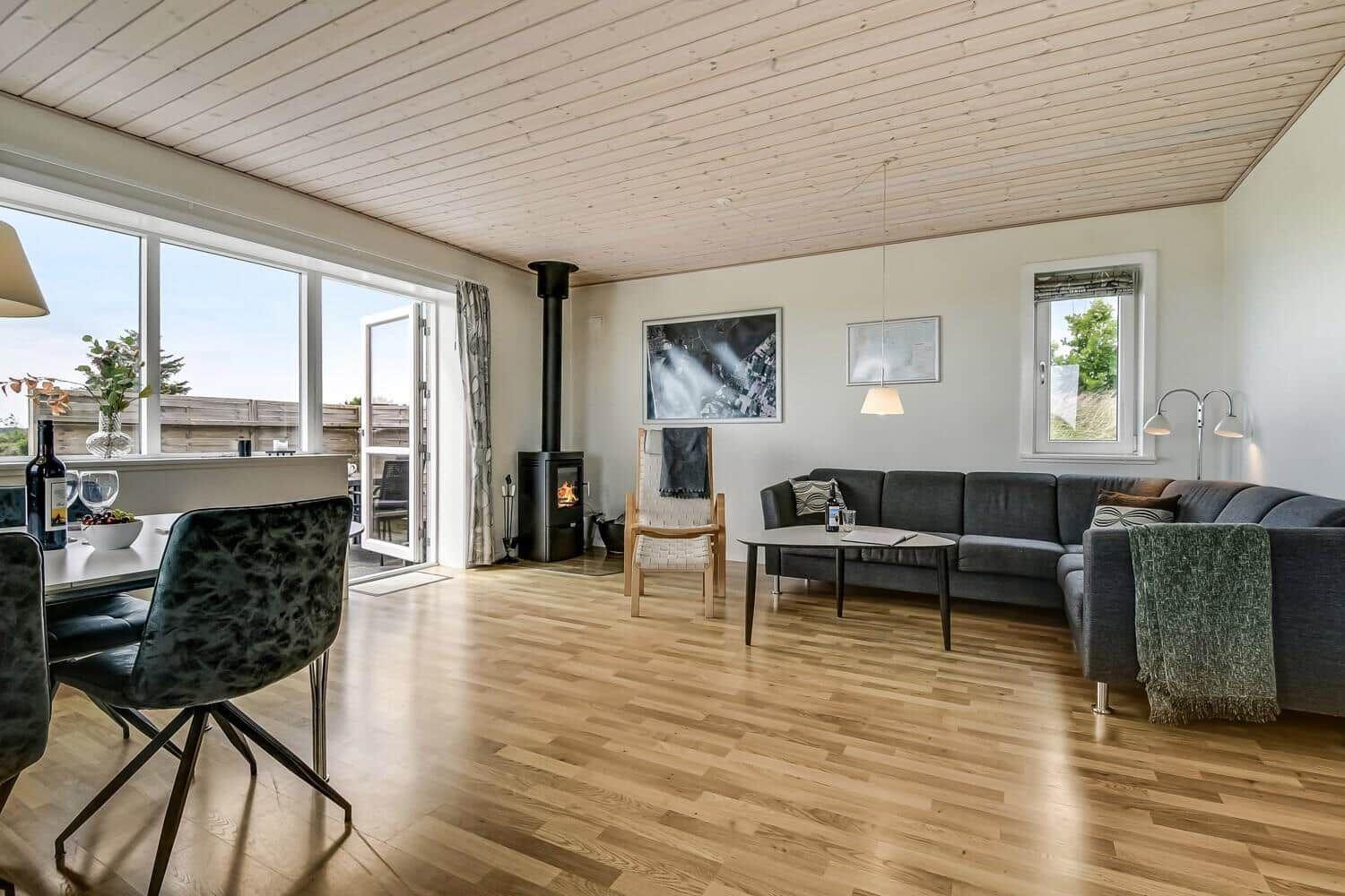 Wohn- und Essbereich mit Holzboden, Sofa, Kamin und großem Fenster.