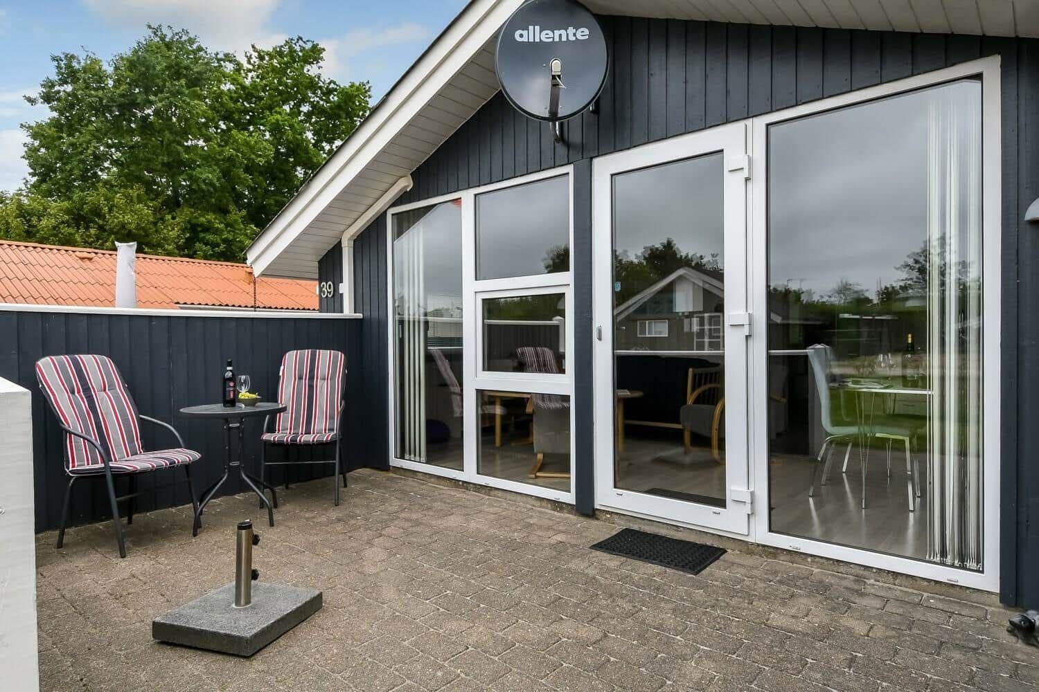 Terrasse mit zwei Stühlen und Tisch vor einem Haus mit Glasfront.