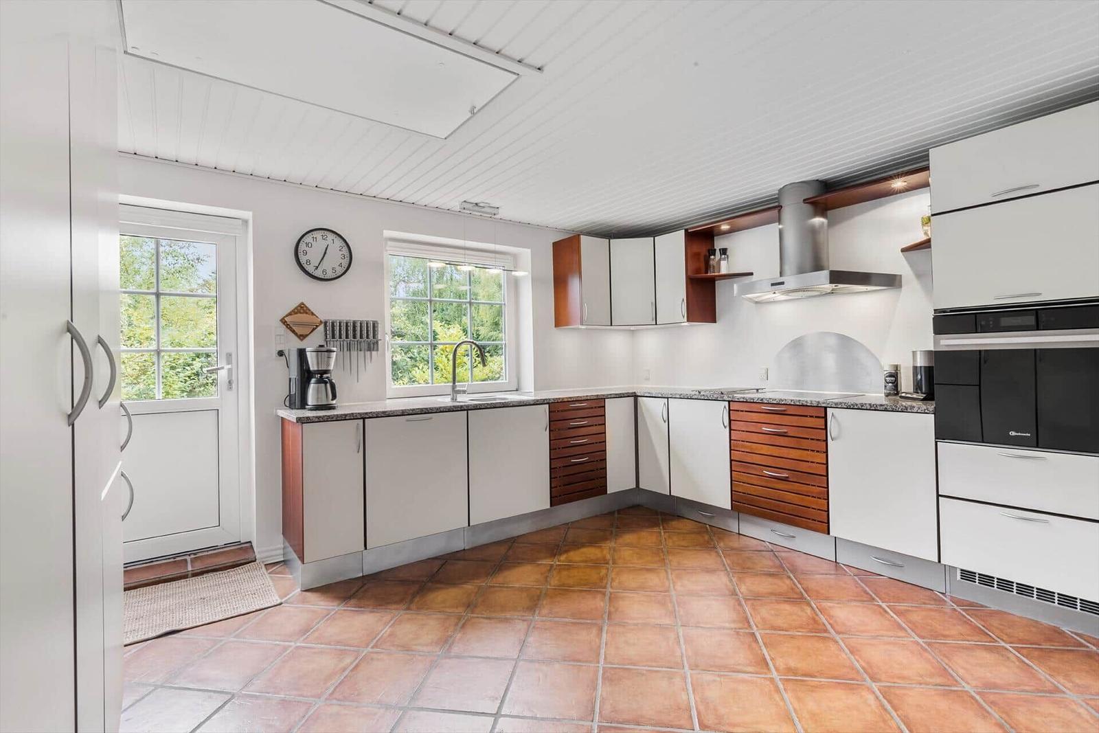 Küche mit weißen Schränken, Holzfronten, Arbeitsplatte und Fenstern.