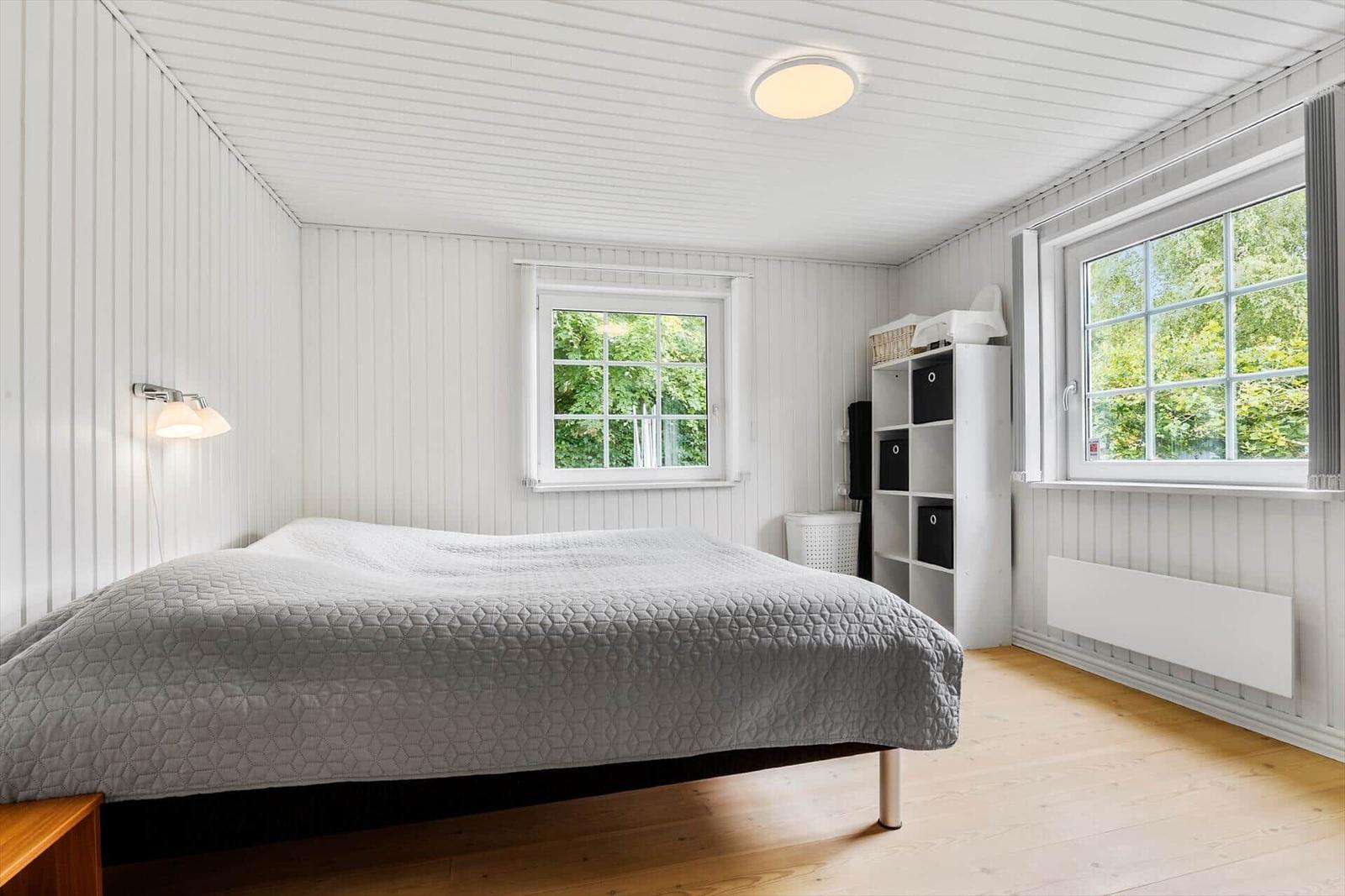 Schlafzimmer mit Bett, Fenstern und Holzboden.