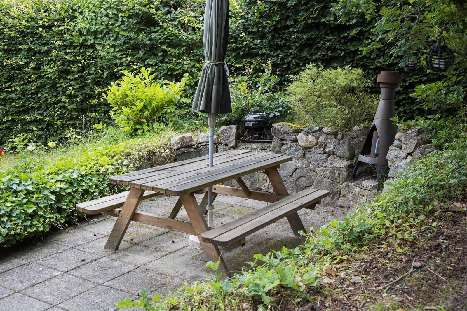 Holztisch mit Bänken, Grill und Feuerkorb im Garten.