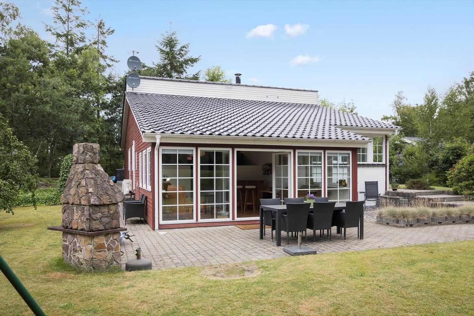 Haus mit Terrasse, Grill und Garten. Große Fensterfront zur Außenseite.