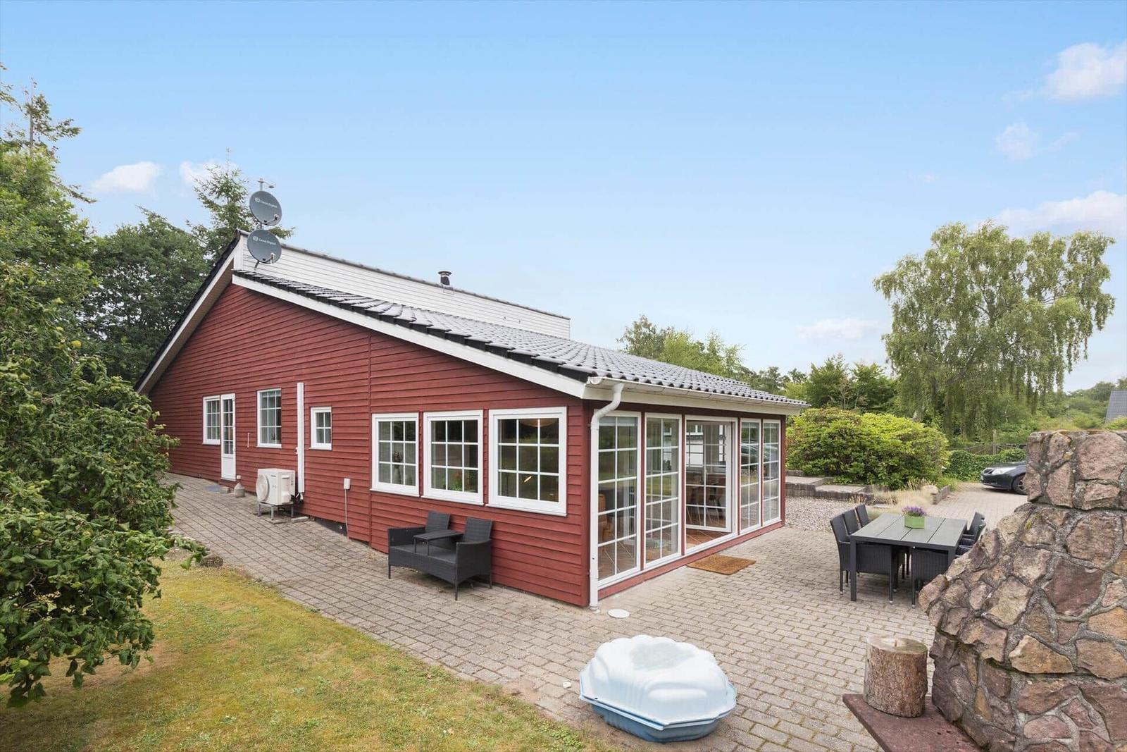 Rotes Haus mit Glasveranda, Terrasse und Garten. Außentisch, Sitzgelegenheiten und Whirlpool.