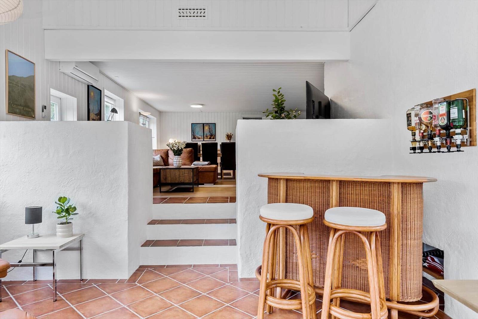 Barbereich mit Hocker und Getränkehalter, Blick in Wohnzimmer mit Sofa und Treppe.