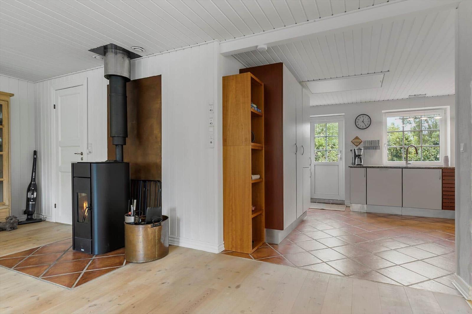 Wohnbereich mit Kaminofen und Küche mit Fenstern.