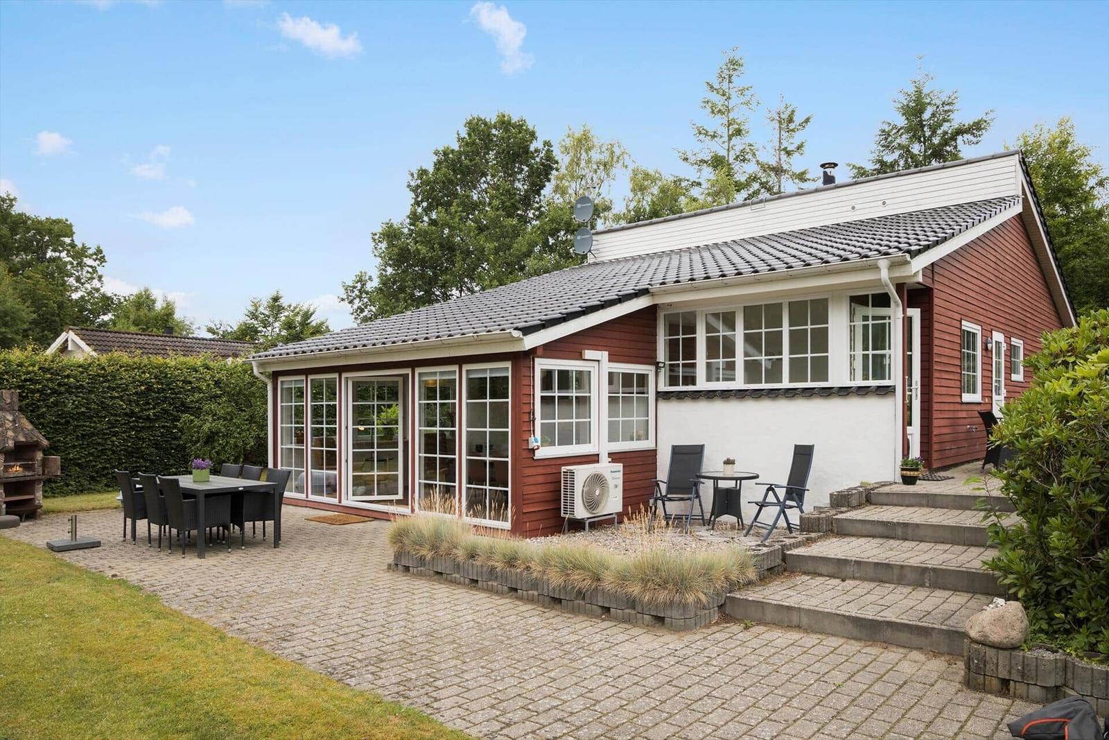 Roter Holzhaus mit Terrasse und Gartenbereich mit Sitzgelegenheiten.