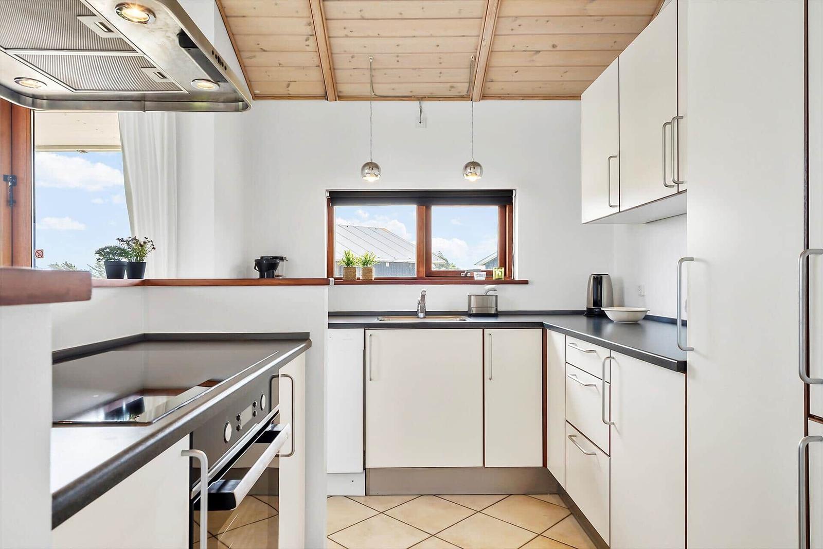 Küche mit weißen Schränken, dunklem Arbeitsplatz und Holzdecke.